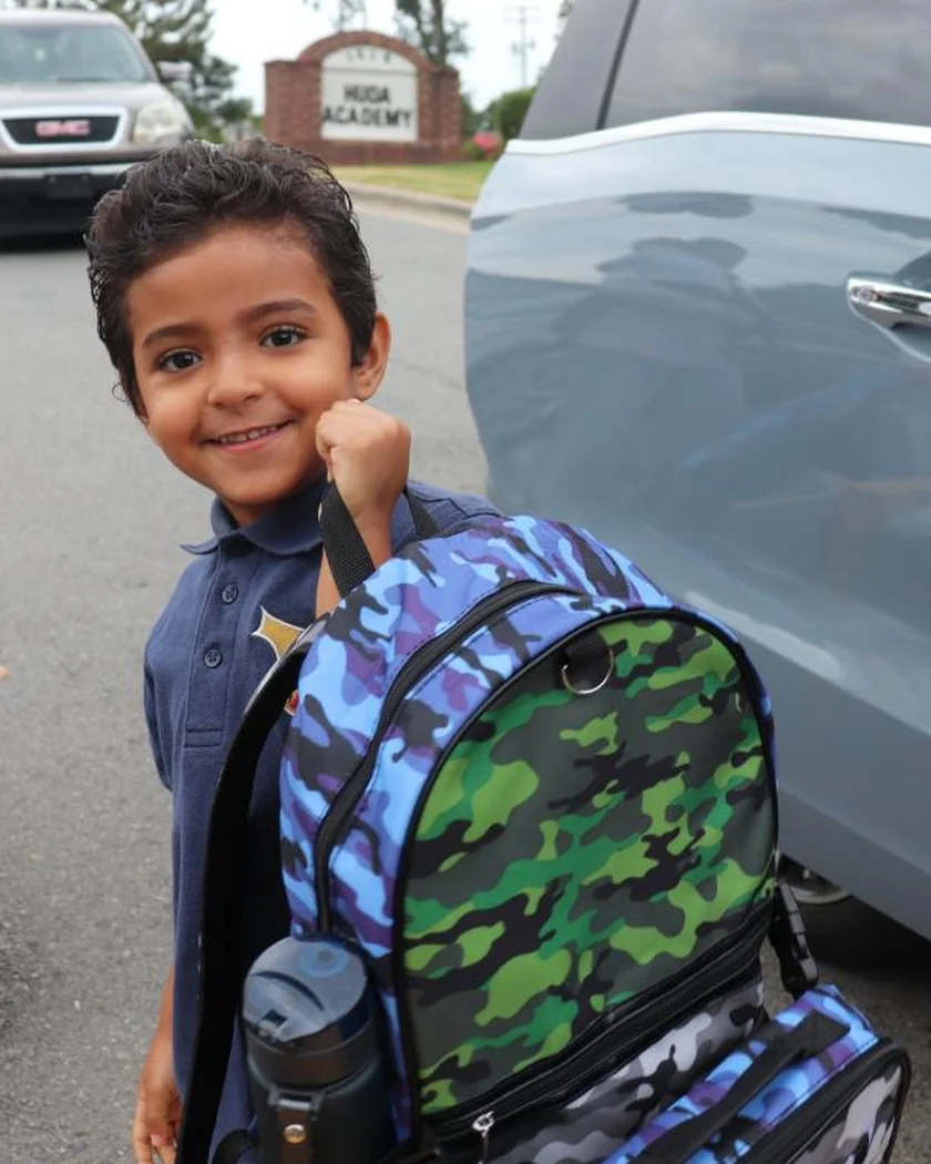 A young student with his backpack at the school sign on the first day